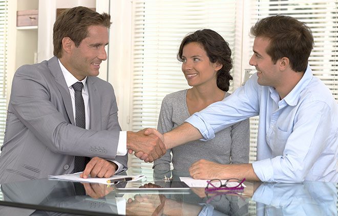 A real estate agent shaking hands with a couple after finalizing a sale
